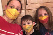 Eine Frau und zwei Kinder tragen selbstgenähte Mundmasken in gelb, rot und grün gemustert