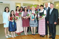 Vier Frauen mit weißem Oberteil und roter Schürze stehen hinter verschiedenen Backformen.