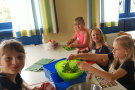 Kinder sitzen um einen Tisch und zupfen Salat in eine Schüssel