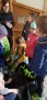 Kinder stehen in bunten Winterjacken vor einer schwarzen Kiste mit Salatpflanzen und Schnittlauch