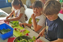 Kinder gießen Gemüsepflanzen in drei Bäckerkisten mit der Gießkanne