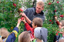 Mann zeigt Kindern Apfelbaum mit reifen Früchten
