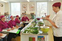 Eine Lehrerin zeigt den Schülerinnen verschiedene Kräuter und deren Unterschiede