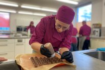 Eine Studierende füllt Pralinenhohlkörper mit einer Ganache in einer Garnierflasche 