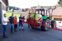 Zwei Frauen und zwei Männer stehen hinter einem Traktor mit Pflanzenschutzspritze