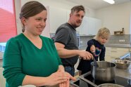 ein einer Küche formt die Mutter Knödel und Vater und Kleinkind rühren in einem Topf.