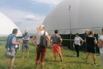 Eine Gruppe von Menschen steht im Gras vor einer kuppelförmigen Biogasanlage