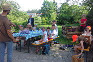 Kinder sitzen auf Biertischen. Am linken Bildrand steht vorne der Bauer und erklärt den Kindern etwas